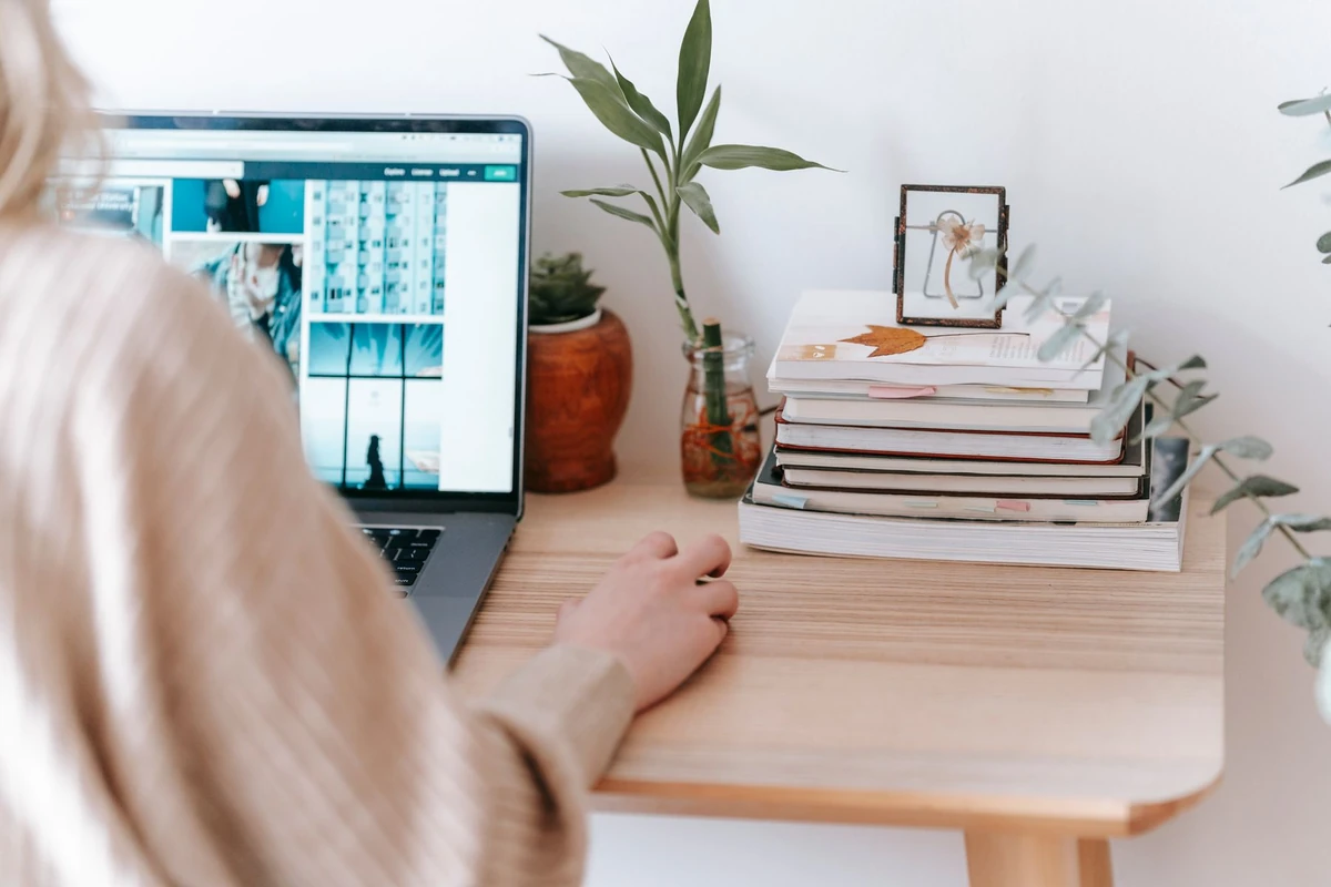 Person using a laptop beside books on a wooden desk