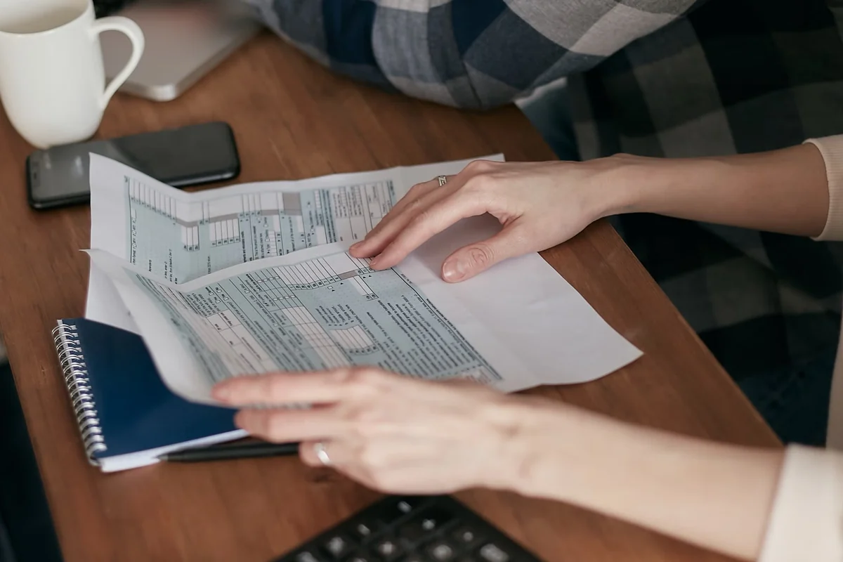 Hands organizing tax forms beside a laptop and calculator