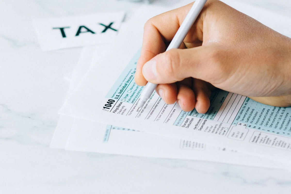 Hand completing a tax form with a pen