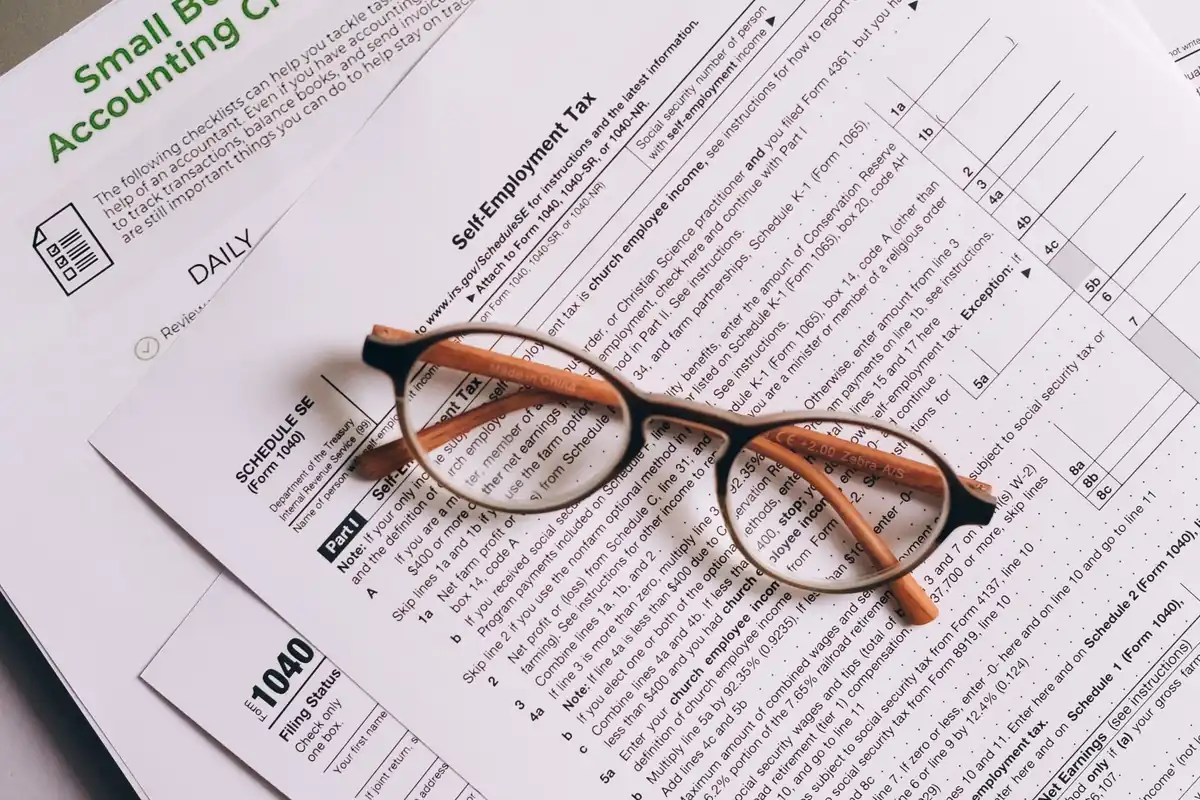 Financial documents and eyeglasses beside a laptop