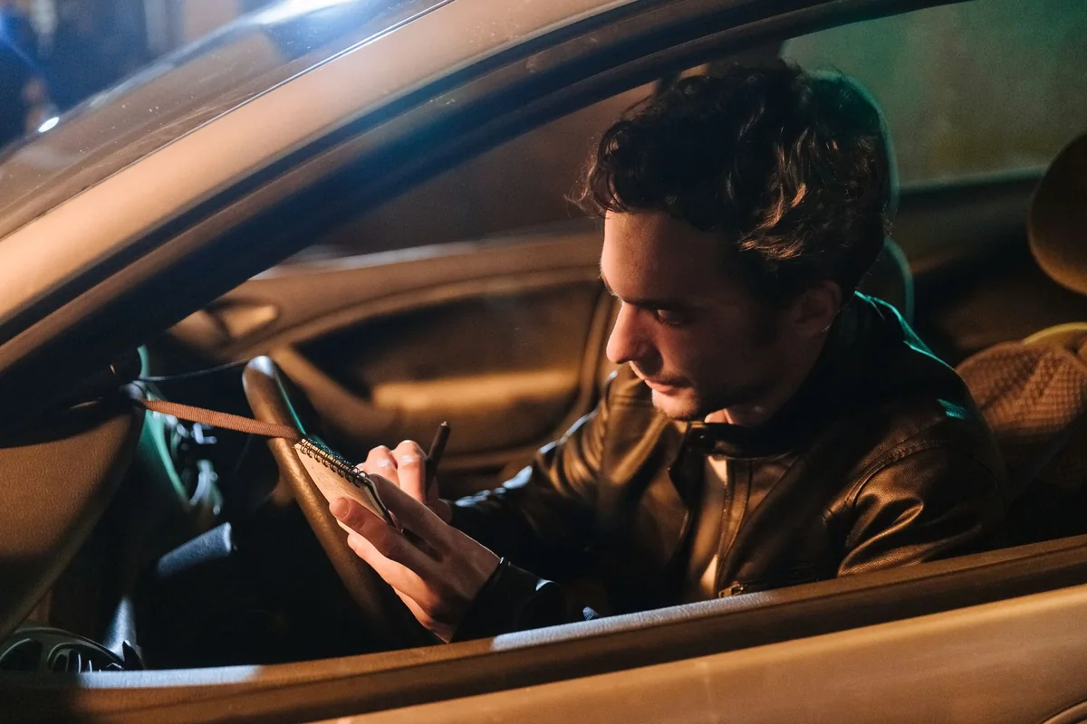 Man writing in a notebook inside a parked car
